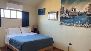 Een slaapkamer met een bed, een airconditioner, een nachtkastje, een lamp en een schilderij.