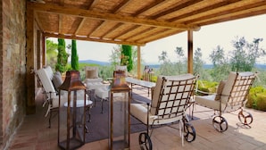 Un espacio de estar al aire libre techado con sillas de mimbre y una mesa, con vistas a un paisaje pintoresco.