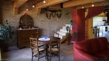 A dining area with a wooden table and chairs, a red sofa, and a kitchen in the background.