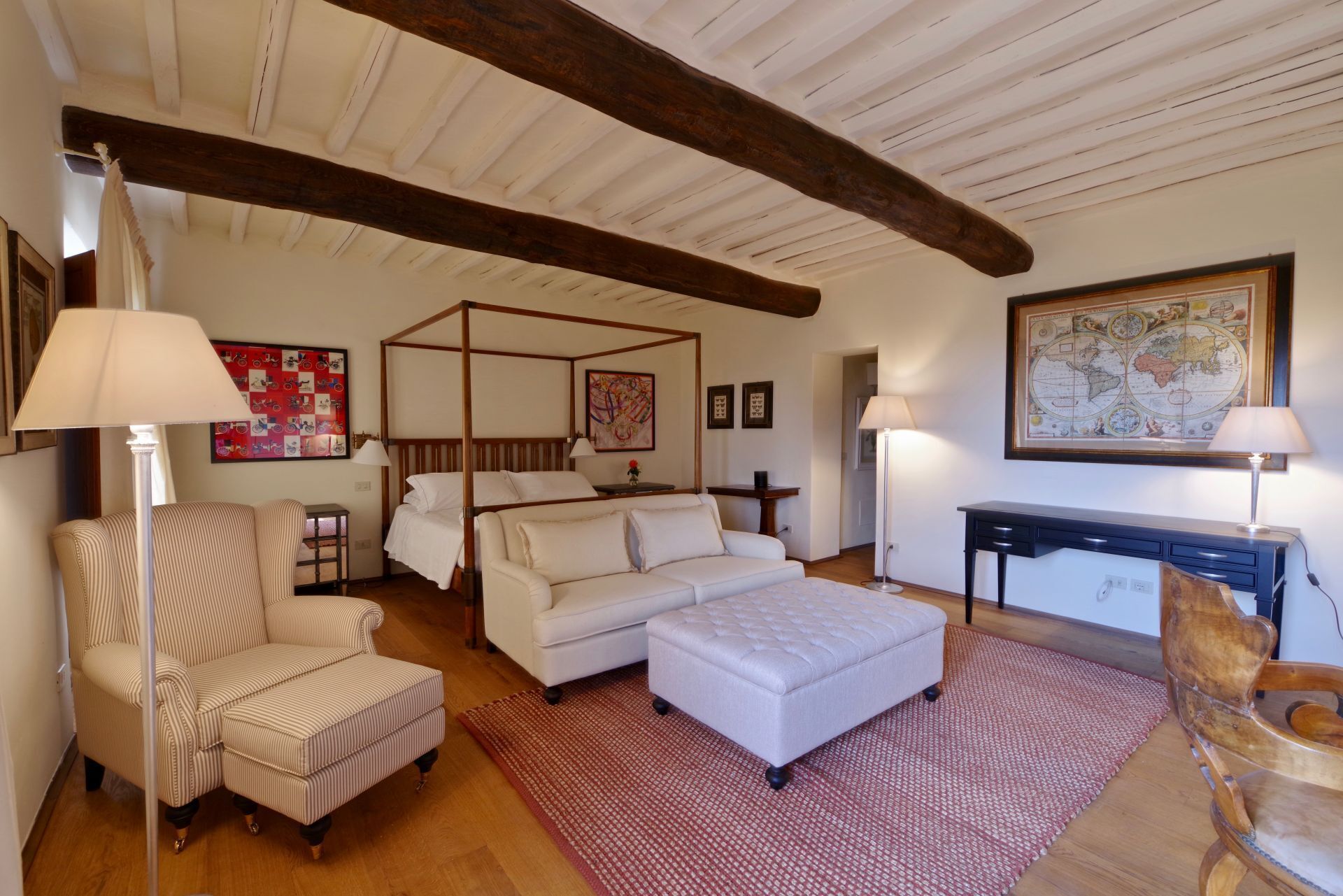Una camera accogliente con un letto a baldacchino, un divano, una poltrona e una scrivania con una lampada.