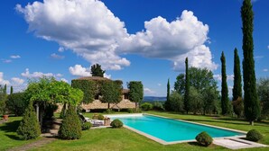 A pool area with a stone structure, surrounded by well-maintained grass and cypress trees. - Camparone Light by ArcenoRentalsClub Magnificent Chianti Villa Pool Concierge (Castelnuovo Berardenga)
