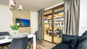 Un salon moderne comprenant un coin repas, un canapé, un téléviseur fixé sur un mur en briques et une vue à travers une porte vitrée.