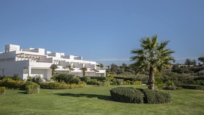A modern white building with multiple levels and balconies, surrounded by well-maintained gardens and palm trees. - Cristina by Interhome (Conil de la Frontera)