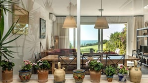 A spacious dining area with a large table, multiple chairs, and a view of the ocean. There are several potted plants on the windowsill. - Cristina by Interhome (Conil de la Frontera)
