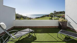 A balcony with a view of the ocean, a lawn, and a seating area with chairs and a table. - Cristina by Interhome (Conil de la Frontera)