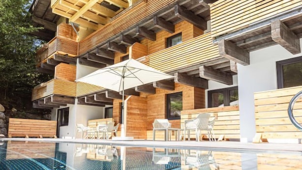 A modern outdoor pool area with wooden deck seating and a glass barrier. - Suite mit 2 SZ & Wellnessbereich by Interhome (Saalbach-Hinterglemm)