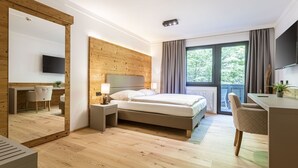 A modern hotel room with a wooden accent wall, a bed, a desk, and a large window with curtains. - Suite mit 2 SZ & Wellnessbereich by Interhome (Saalbach-Hinterglemm)