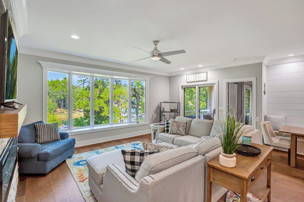 A spacious living room with large windows, a ceiling fan, and a view of a lake.