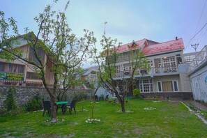 A courtyard with a stone wall, green grass, and a few trees. There are outdoor tables and chairs.