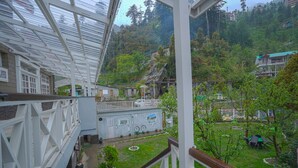 A view from a balcony overlooking a courtyard with a green lawn, a small garden, and a building with a mural. - Boho Mansion - by Dumnu Homes (Manali)