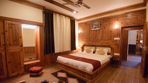 A wooden-paneled bedroom with a large bed, a ceiling fan, a mirror, and a nightstand. - Boho Mansion - by Dumnu Homes (Manali)