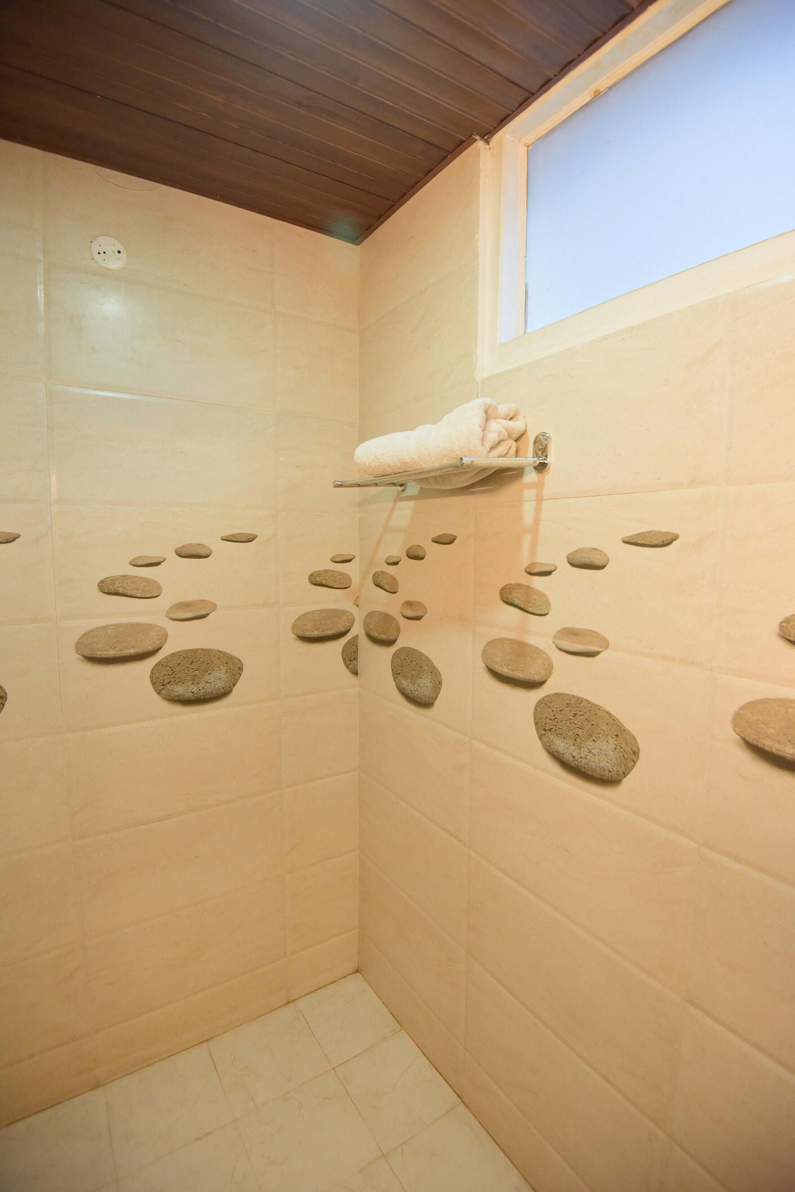 A bathroom with beige tiles, a towel rack, and a window.