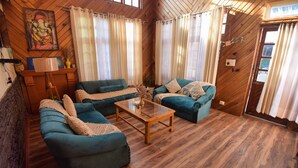 A cozy living room with two teal sofas, a wooden coffee table, and a wooden floor. - Boho Mansion - by Dumnu Homes (Manali)