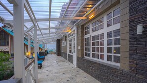 A covered corridor with stone walls and large windows, leading to a building entrance. - Boho Mansion - by Dumnu Homes (Manali)