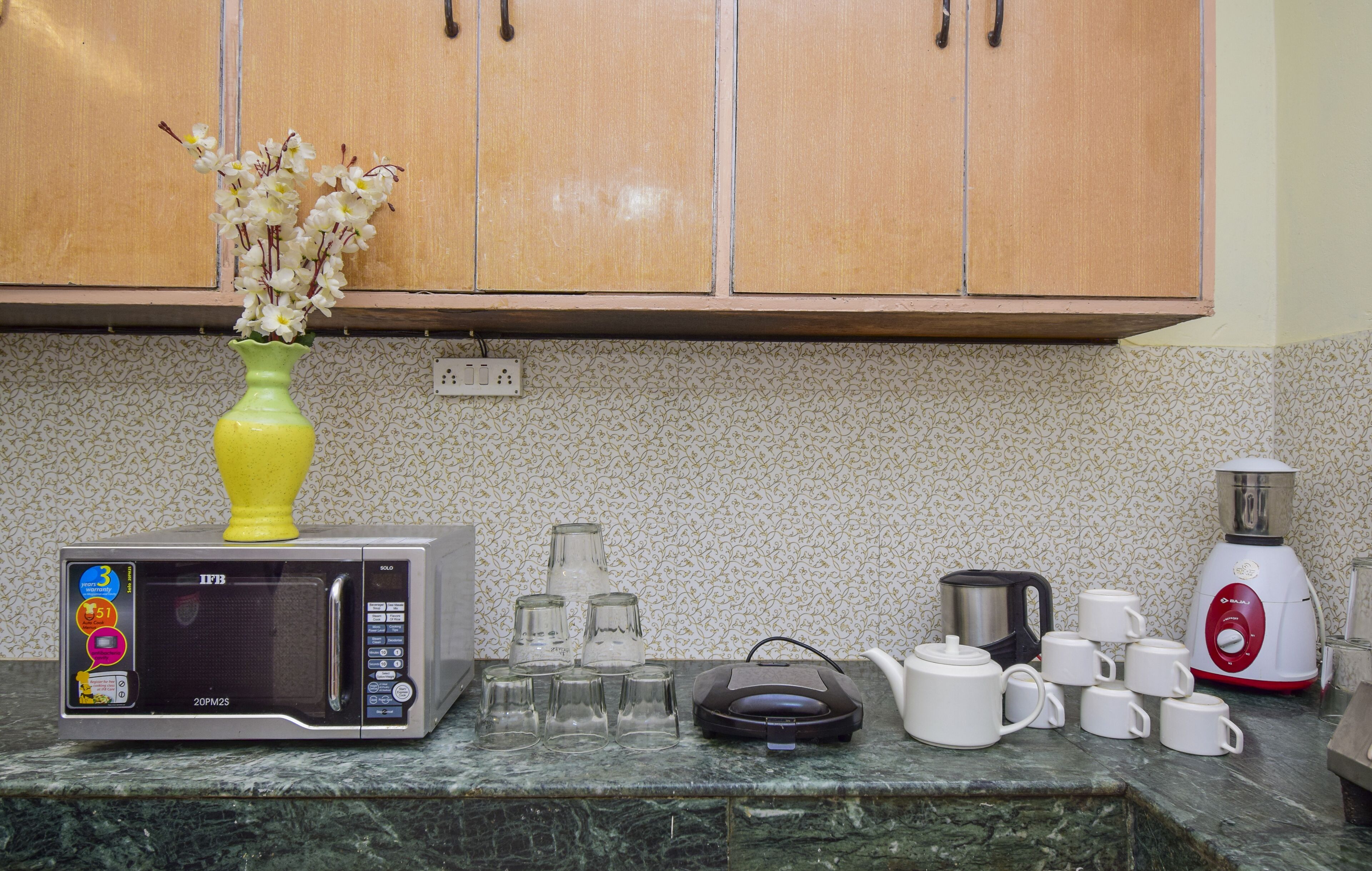 Een keuken met een magnetron, een koffiezetapparaat en een vaas met bloemen op het aanrecht.