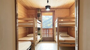 Ein Zimmer einer Holzhütte mit Etagenbetten, Fliesenboden und einem Balkon mit Bergblick.