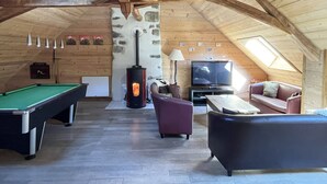 Ein gemütliches Dachzimmer mit Billardtisch, Sofa, Fernseher und Holzofen.