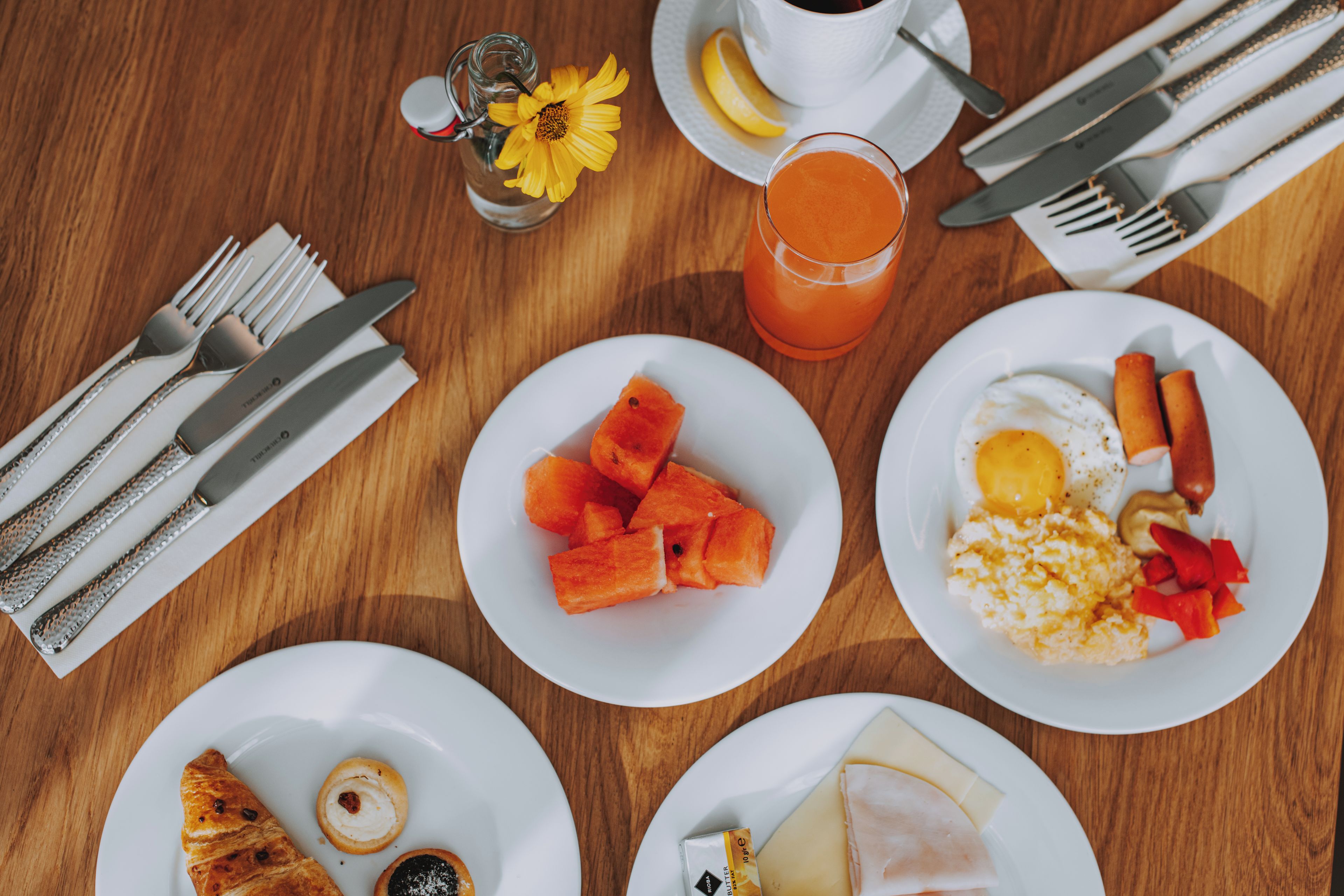 A breakfast setting with plates of food, a glass of juice, and cutlery on a wooden table.