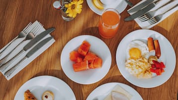 A breakfast setting with plates of food, a glass of juice, and cutlery on a wooden table.