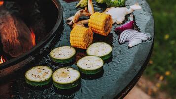 A grill with vegetables and corn on a circular grill surface.