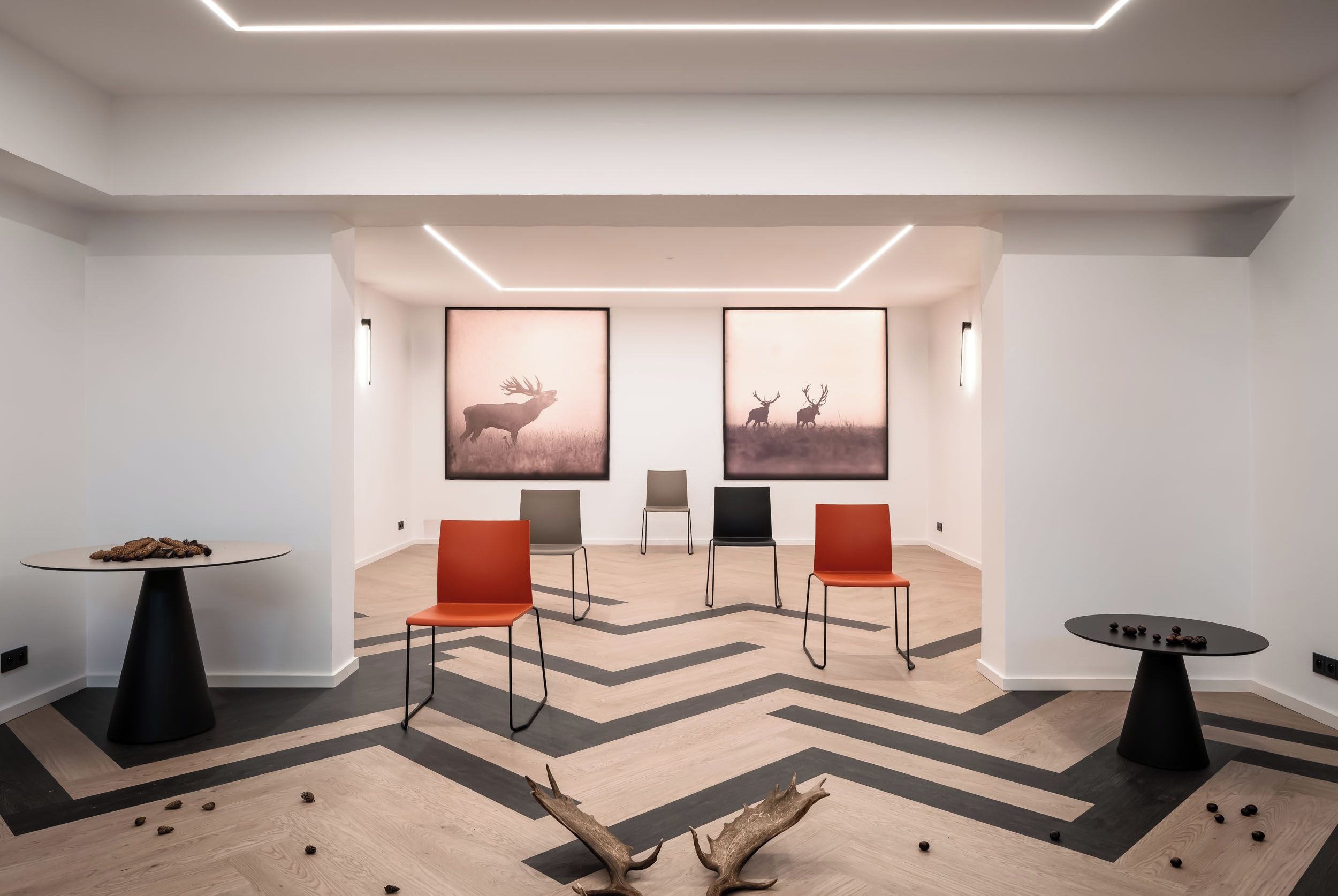 A modern interior with a geometric patterned floor, a central table with a unique base, and two framed wall art pieces depicting deer.