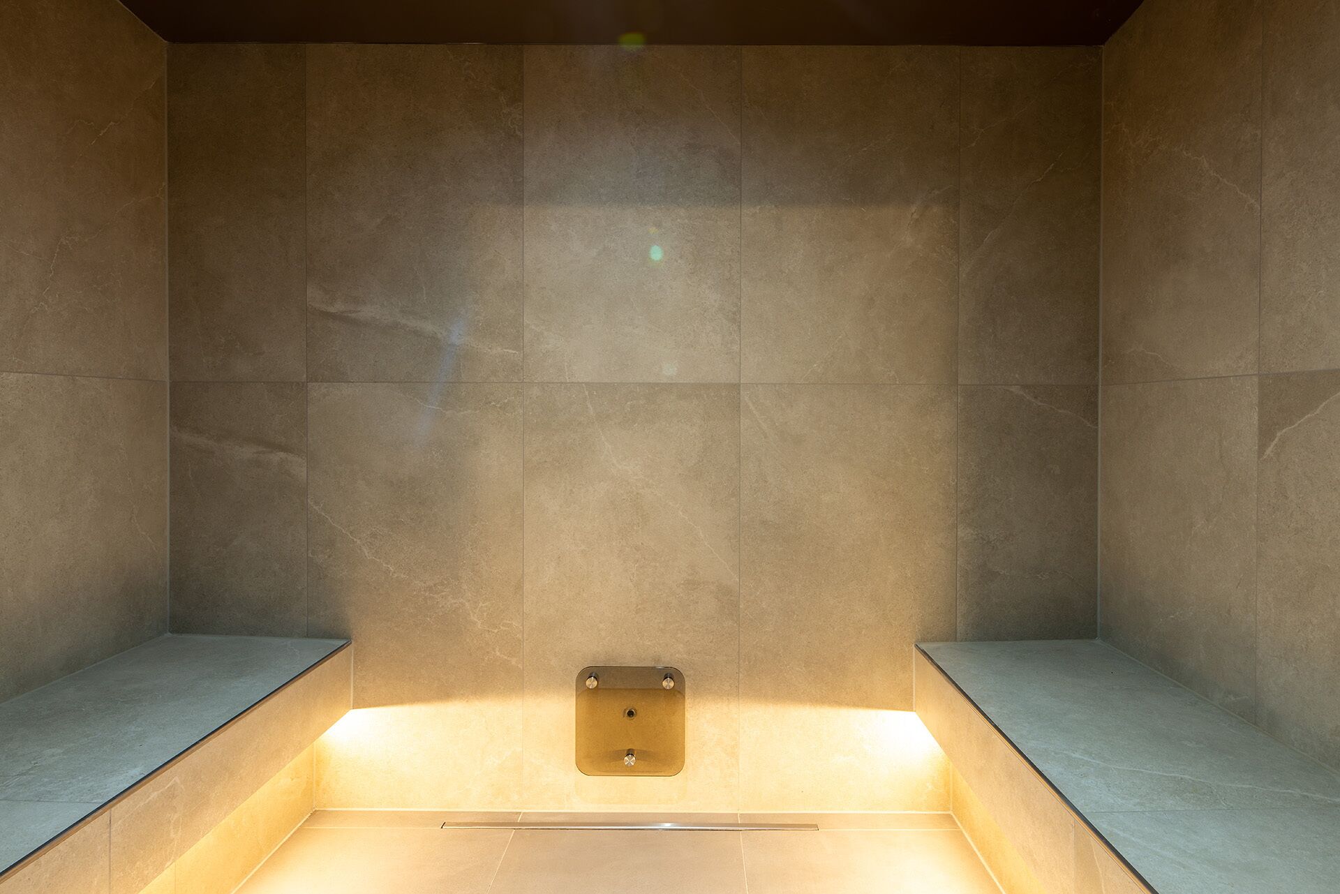 Een spa-ruimte met een rechthoekige bank, een klein wastafeltje en een wandlamp.