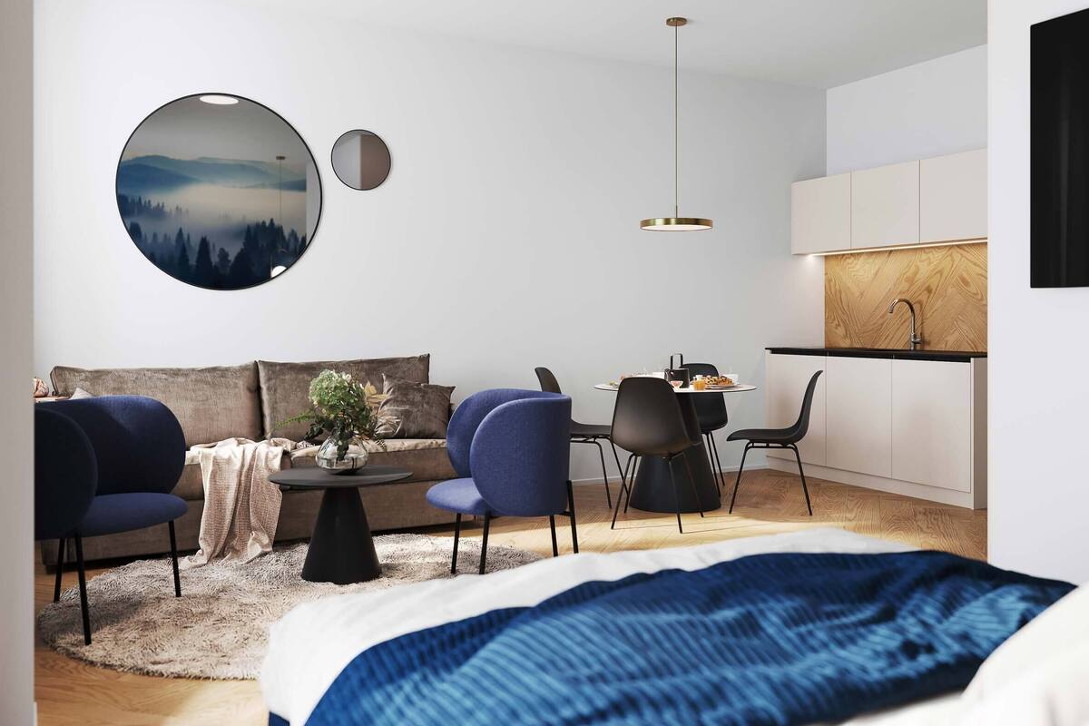 Un dormitorio moderno con cama, espejo redondo, mesa de comedor con sillas y kitchenette.