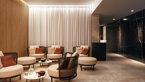 Ein moderner Lounge-Bereich mit Sofas und Sesseln, einem Couchtisch mit Früchten und Gläsern sowie einem großen Fenster mit Vorhängen.