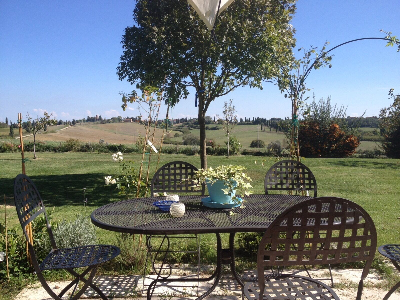 A round metal table with chairs, surrounded by greenery and a view of rolling hills.