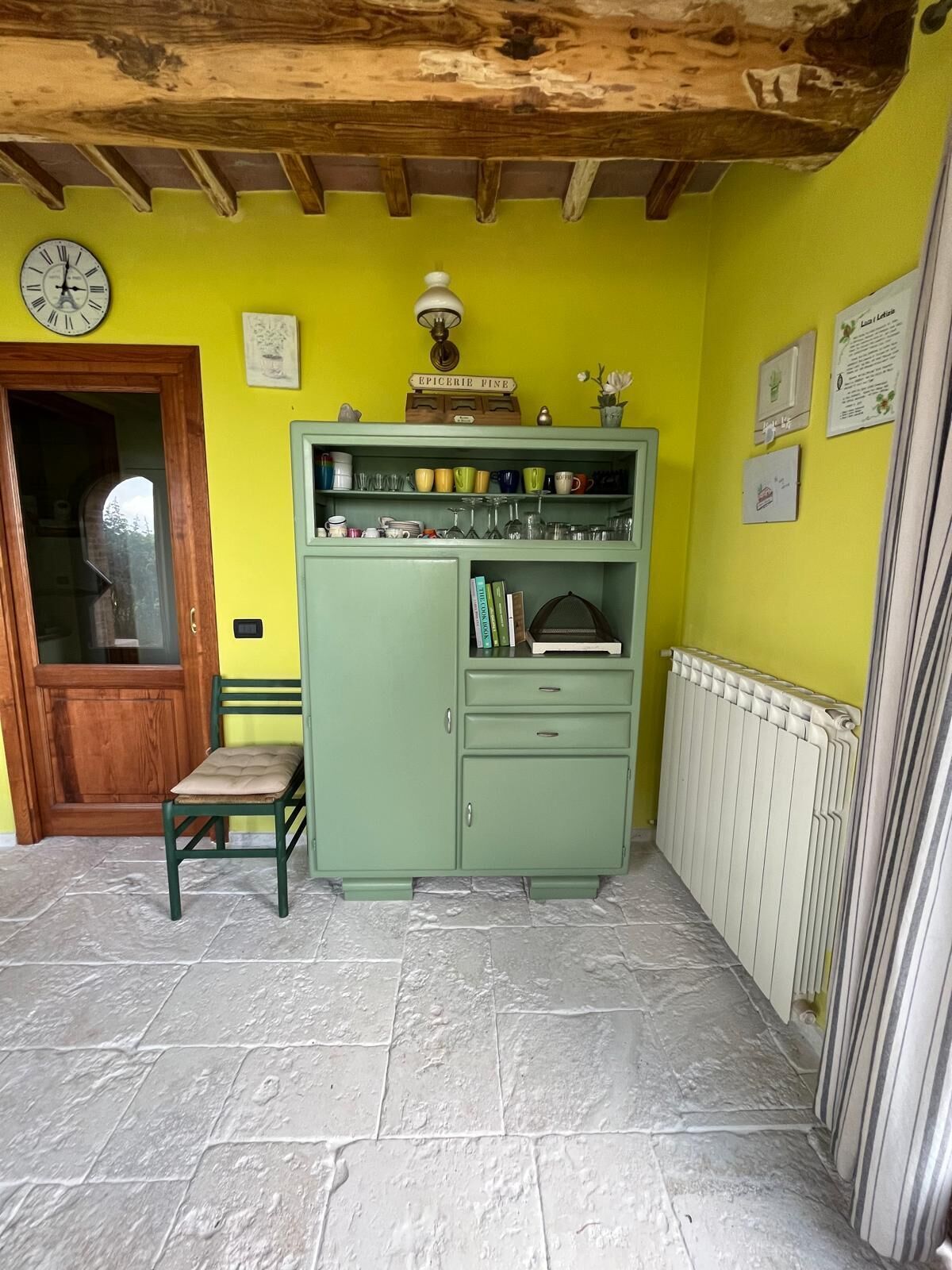 Une pièce avec un meuble vert, une porte en bois, une chaise et un radiateur.