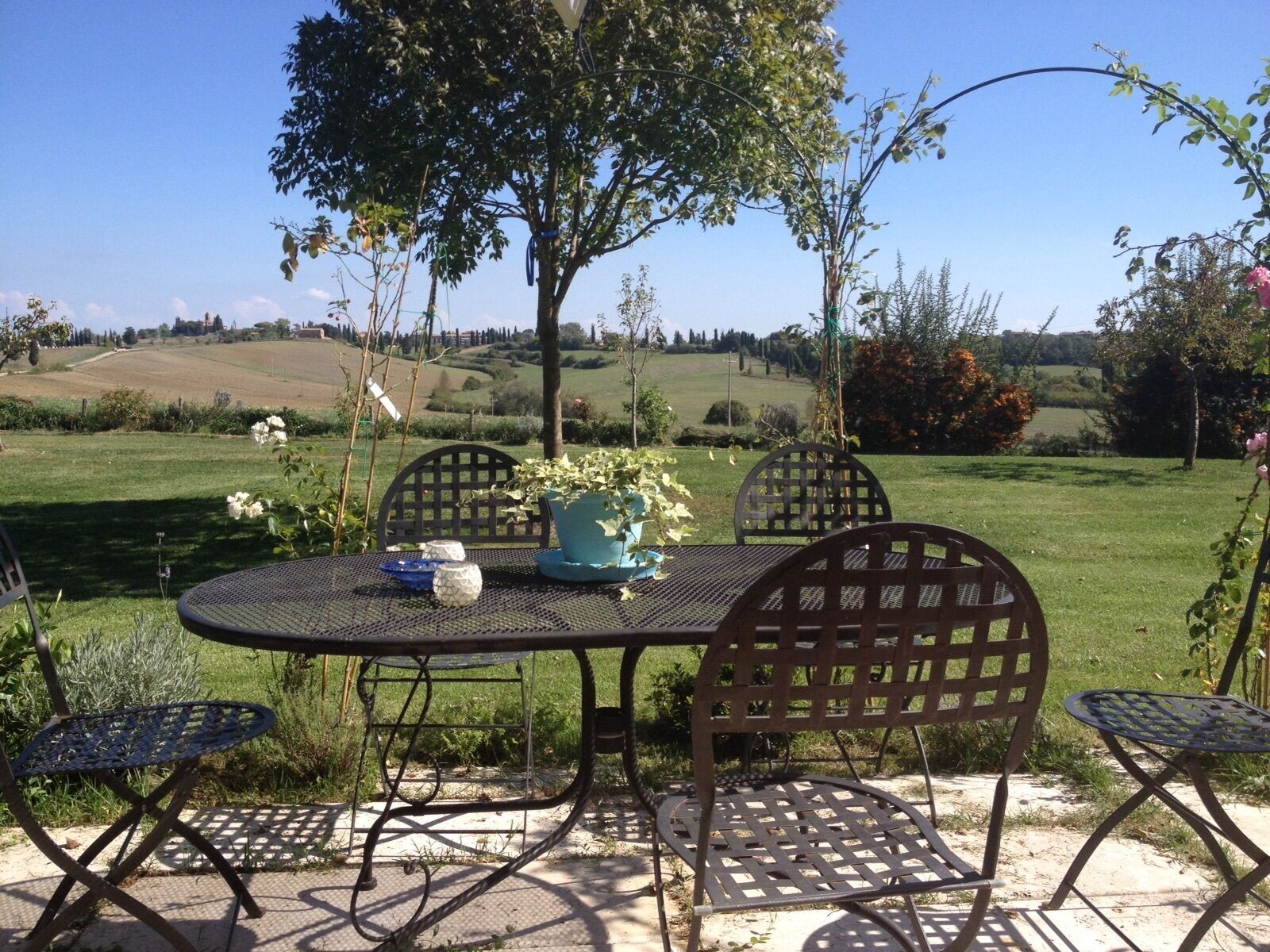Une table et des chaises sont disposées à l’extérieur, offrant une vue sur des collines verdoyantes et des arbres.
