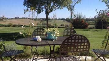 Une table et des chaises sont disposées à l’extérieur, offrant une vue sur des collines verdoyantes et des arbres.