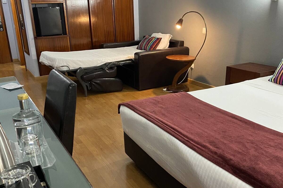 A hotel room with two beds, a desk with a coffee maker, a TV, and a wardrobe.