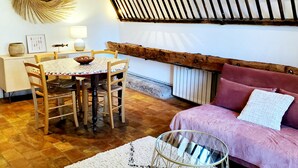 A dining area with a round table and chairs, a sofa, a decorative wall piece, and a staircase with exposed wooden beams. - NICE PROVENCALE HOUSE 4 pers country garden swimming pool SPA playground (Grans)