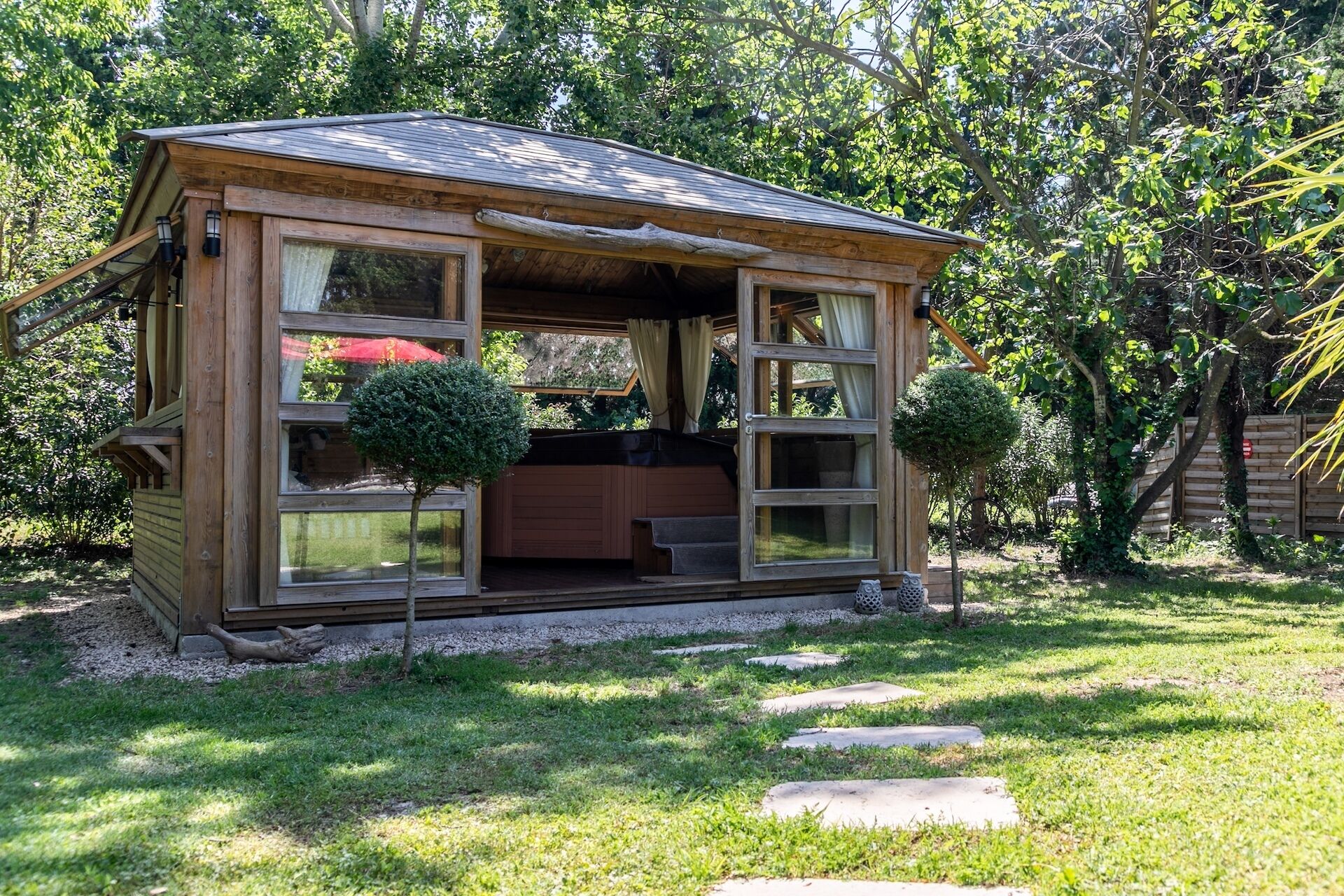 Een houten chalet met grote ramen en een overdekte veranda, omgeven door een tuin en bomen.
