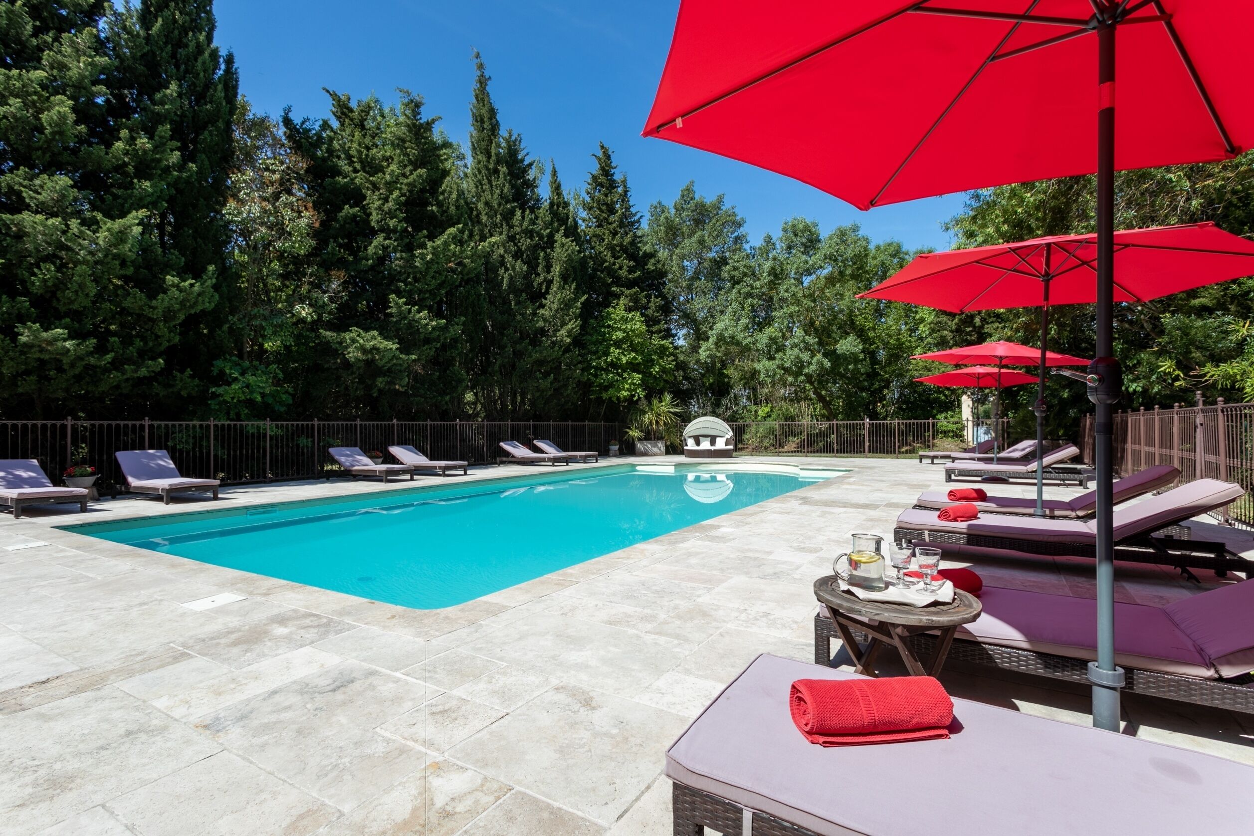 Una piscina amb gandules i ombrelles vermelles, envoltada d'arbres.