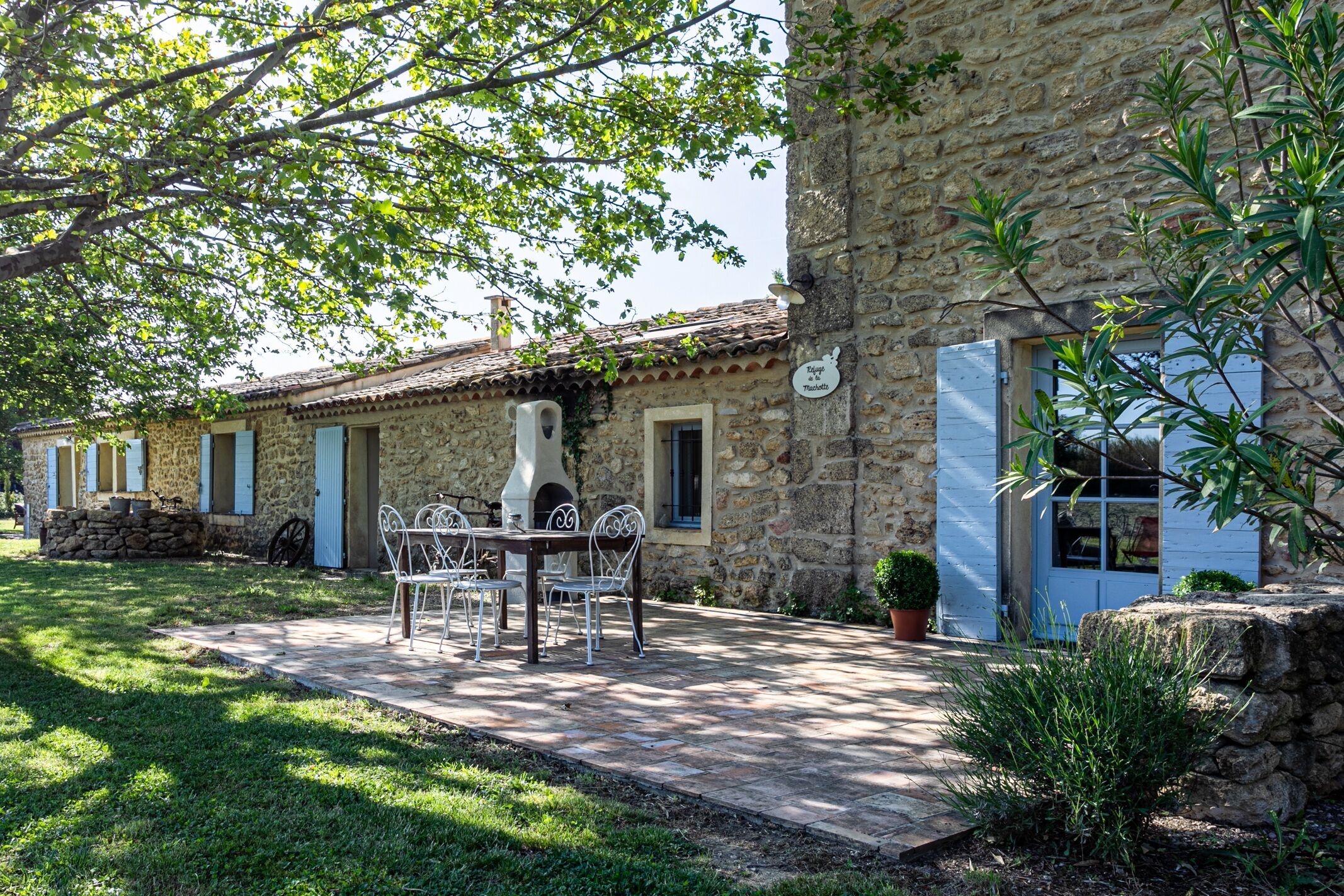 A stone building with a patio area featuring a table and chairs, surrounded by greenery and a stone wall.