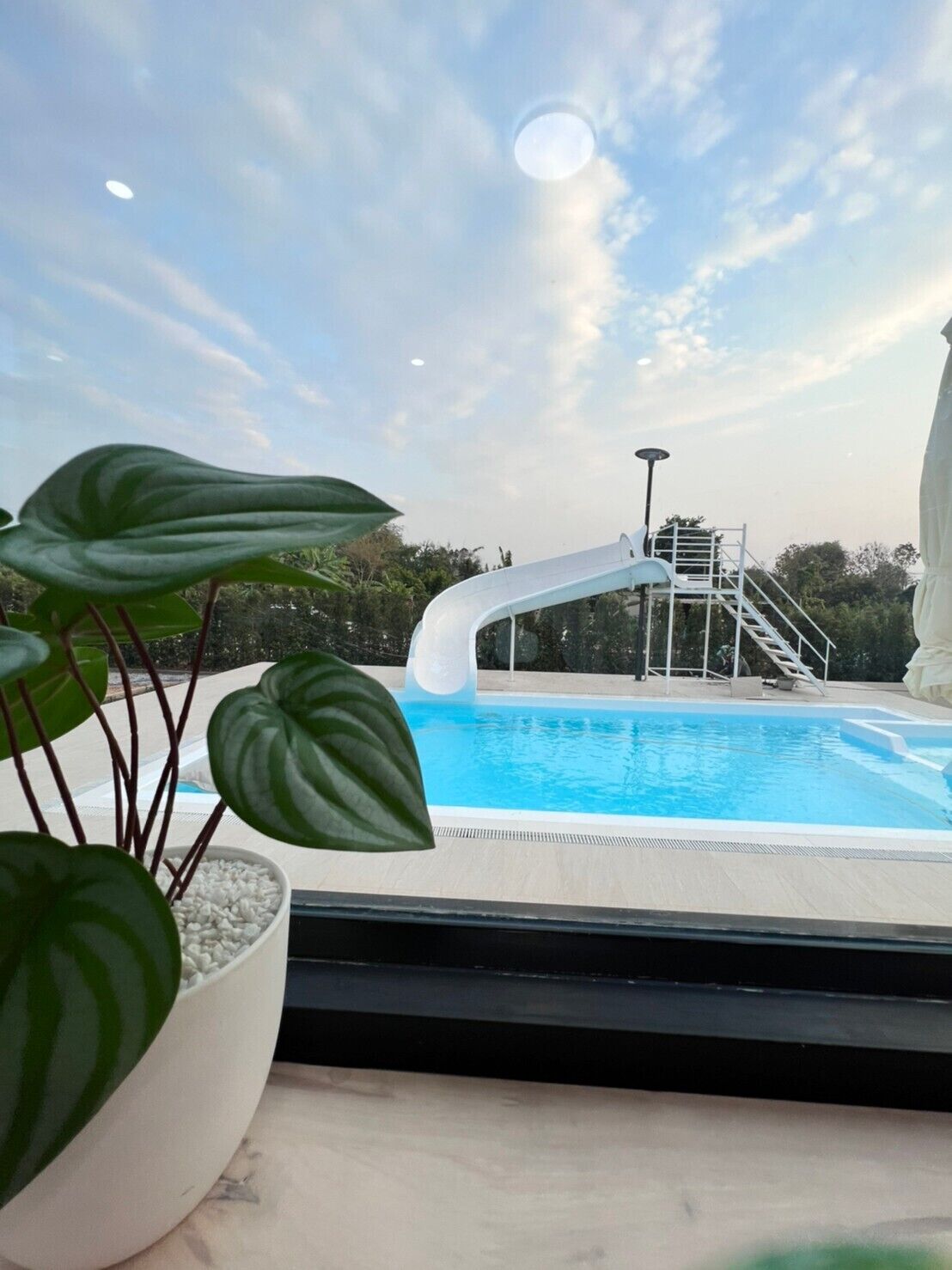 Piscina com escorregador, rodeada por vegetação e céu claro.