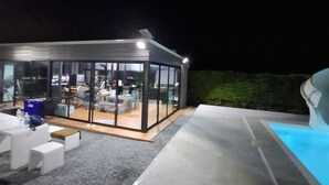 A modern outdoor lounge area with a glass enclosure, outdoor seating, and a pool.