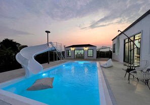 A swimming pool with a slide, a covered seating area, and a building with a circular window in the background. - Private home, pool villa , 4 k.m. from airport (Tambon Ban Du)
