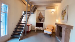 A living room with a staircase, a fireplace, a chair, and a painting on the wall. - Private Pool in Cottage (POROS)