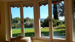 A room with a bay window overlooking a green lawn and trees. - Private Pool in Cottage (POROS)
