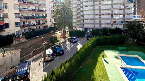 A residential building with multiple balconies, a swimming pool, and a parking area with cars. - DON PACO  (2 BEDROOMS) (Benidorm)