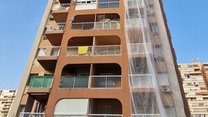 A tall residential building with multiple balconies, a clear sky, and a green hedge in the foreground. - DON PACO  (2 BEDROOMS) (Benidorm)