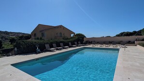Une piscine rectangulaire à l’eau d’un bleu limpide, entourée de carreaux de couleur beige et de chaises longues.