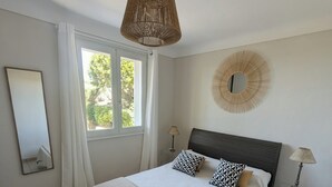 Une chambre avec un grand lit, un luminaire suspendu, un élément de décoration circulaire fixé au mur, une table de chevet avec une lampe et une fenêtre avec des rideaux.