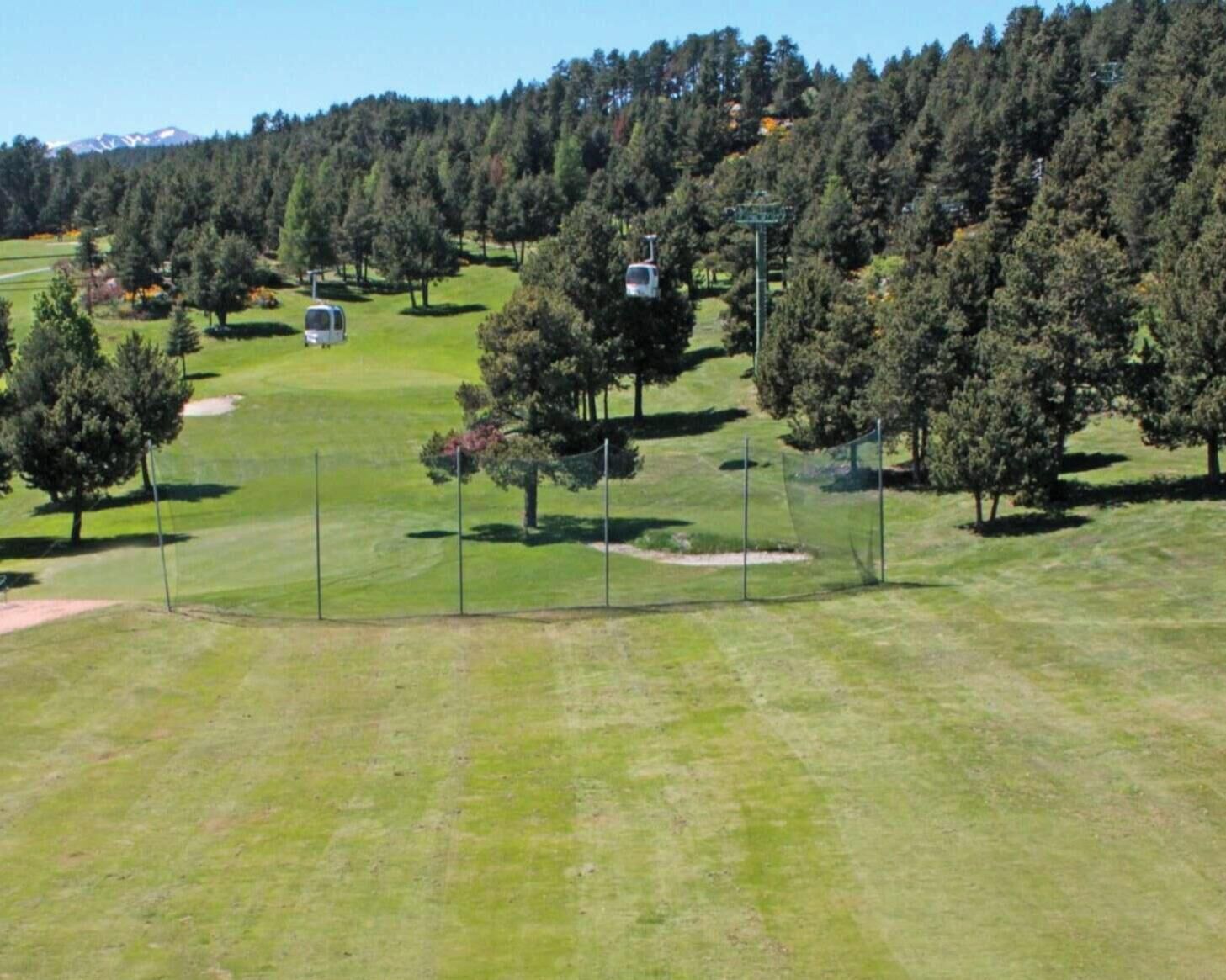 Campo de golf con cielo despejado, árboles y una montaña distante.