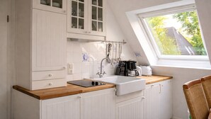 A kitchen with white cabinets, a wooden countertop, a sink, and a window with a view of trees.
