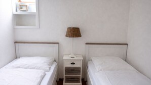 A small, clean room with two single beds, a nightstand with a lamp, and a white wall.