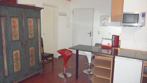 Eine Küche mit einem Holzkasten, einem roten Barhocker, einem weißen Kühlschrank und einer Mikrowelle.